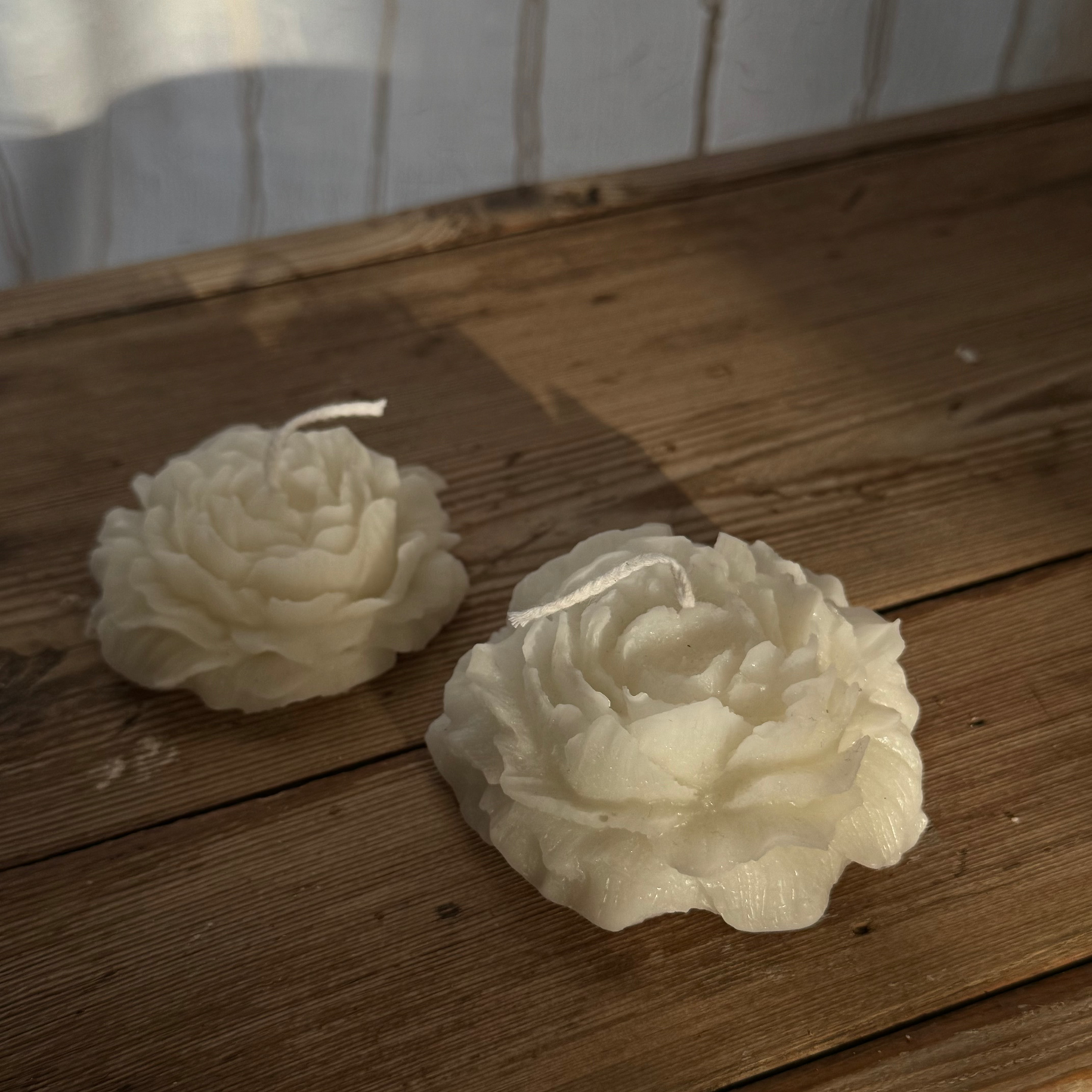 Two white flower-shaped candles on a wooden surface with a white wall in the background.