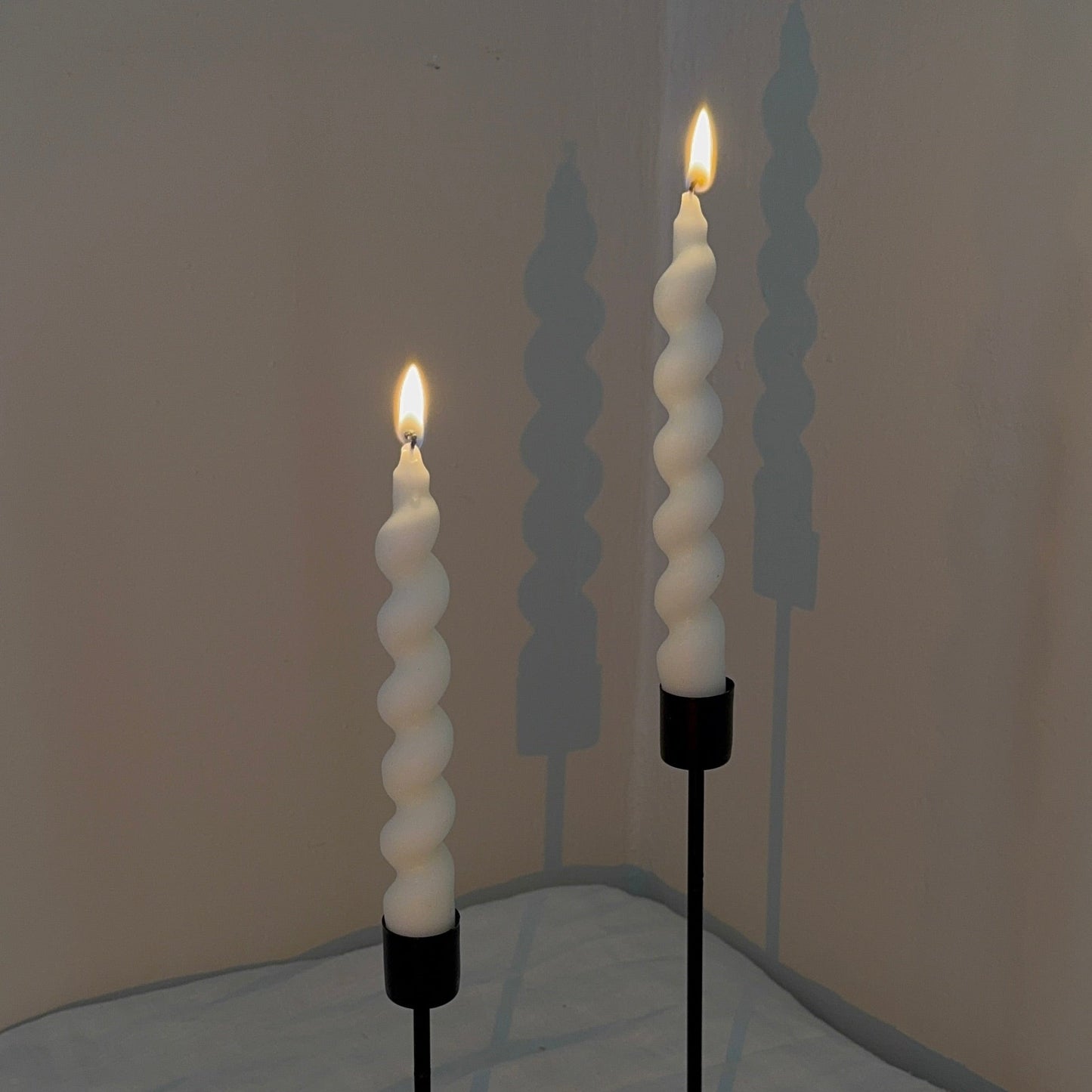 Two spiral candle holders with lit candles on a neutral background