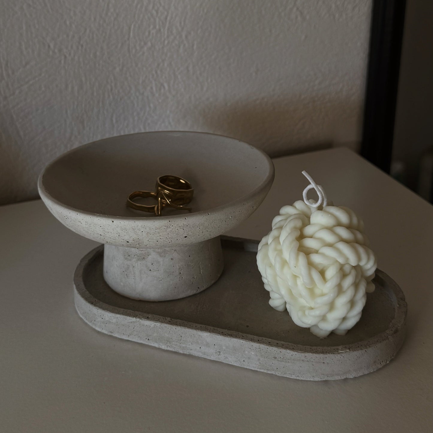 A minimalist concrete ring holder that doubles as a wax melt holder, displayed with rings on the top and a wax melt shaped like a flower on the side.