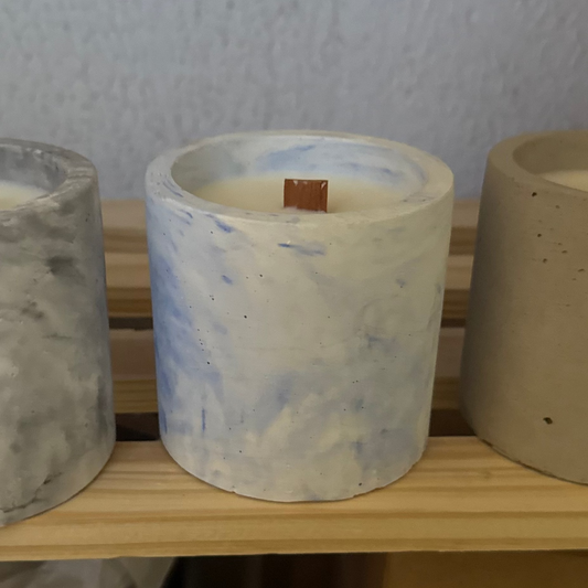 Cylindrical candle with marbled patterns on a wooden shelf.
