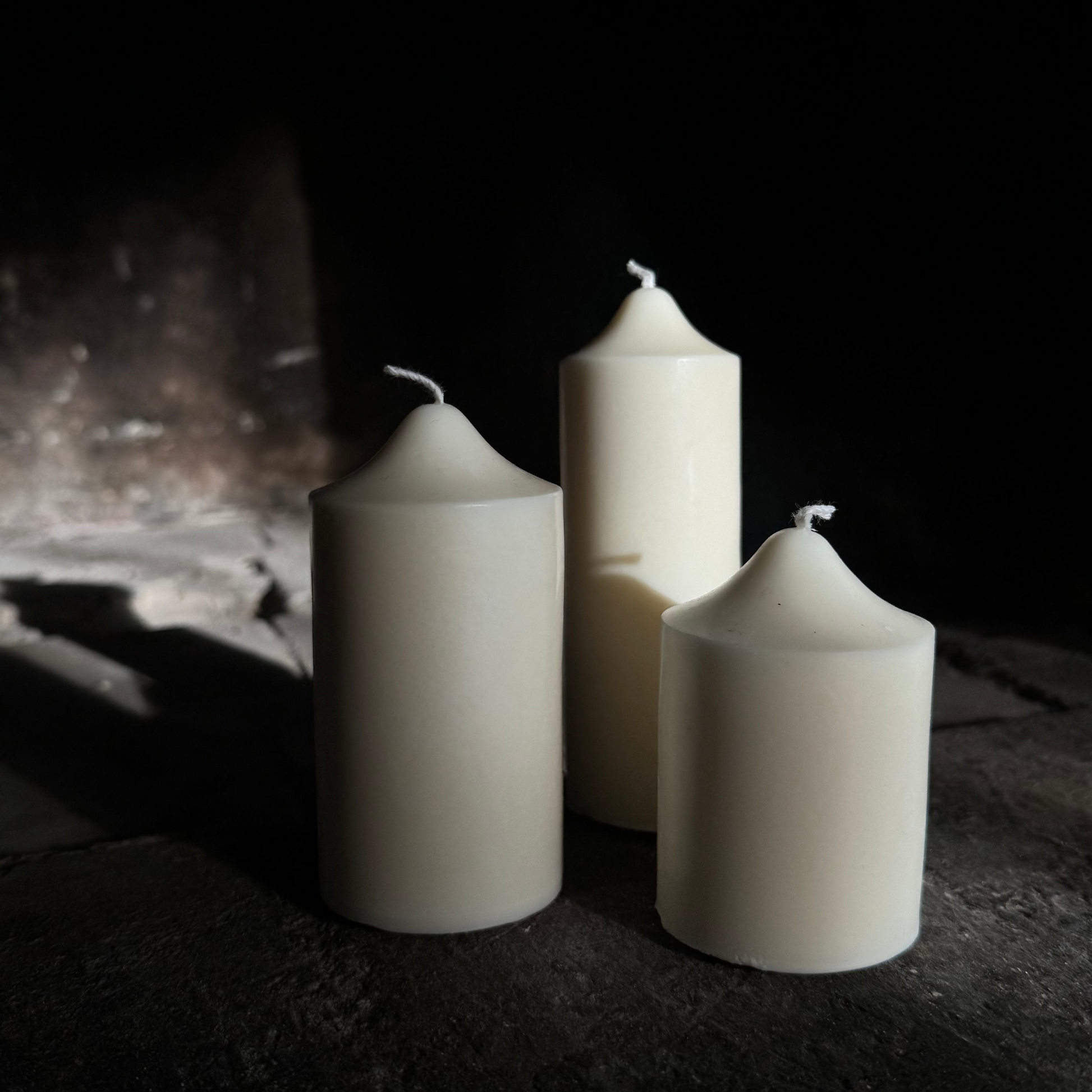 Three white candles on a dark surface with a dark background