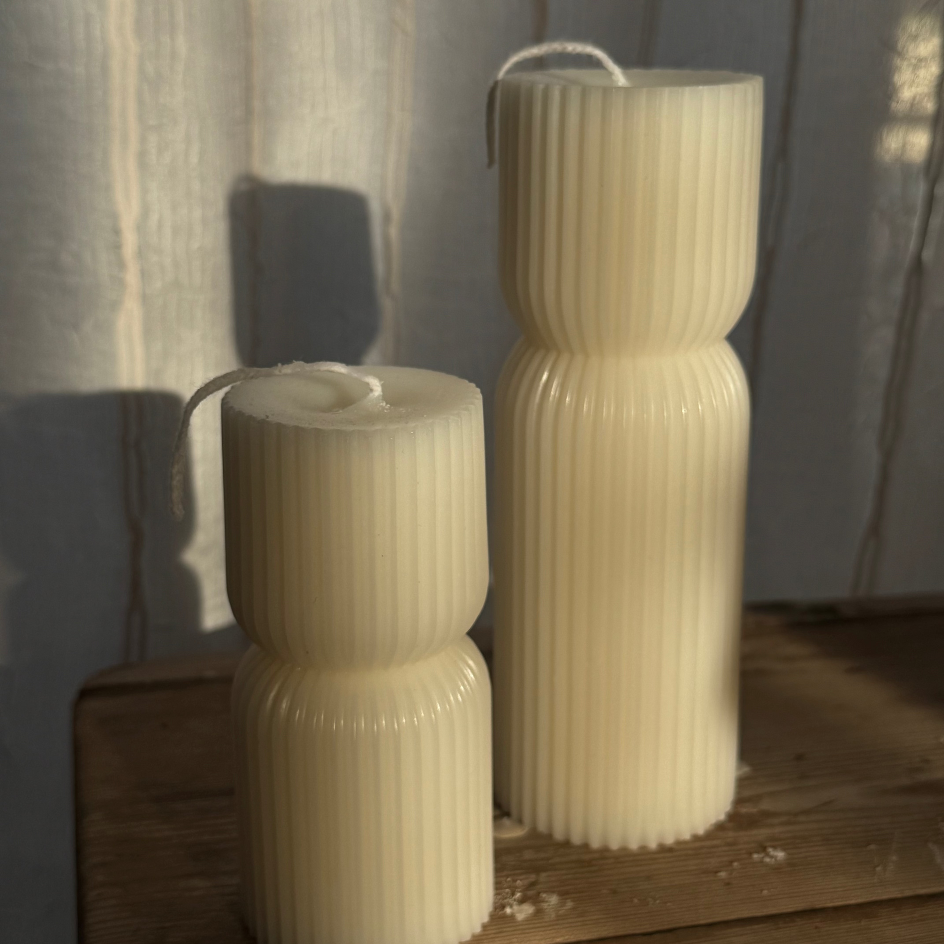 Two ribbed candles on a wooden surface with a soft, diffused light.