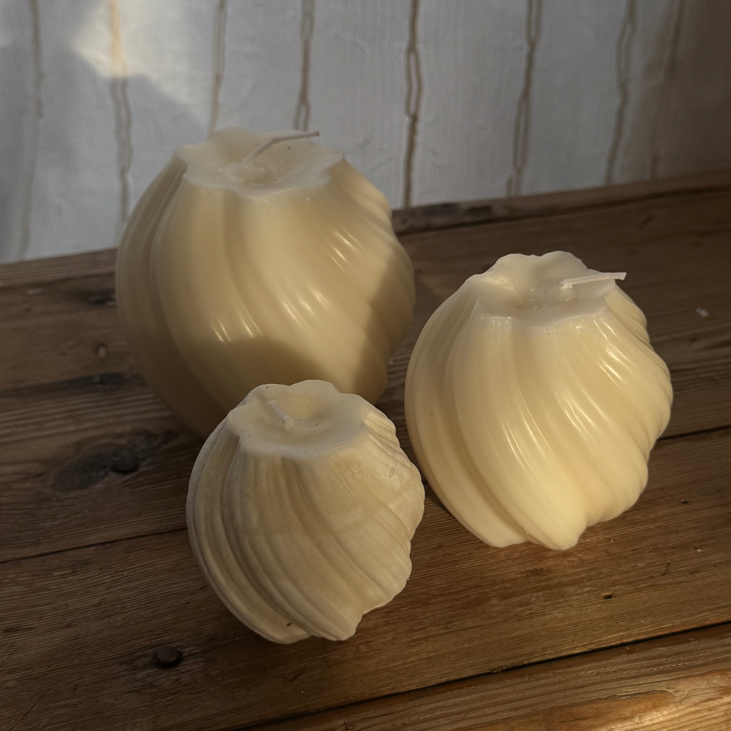 Three white spherical candles on a wooden surface with a white textured background