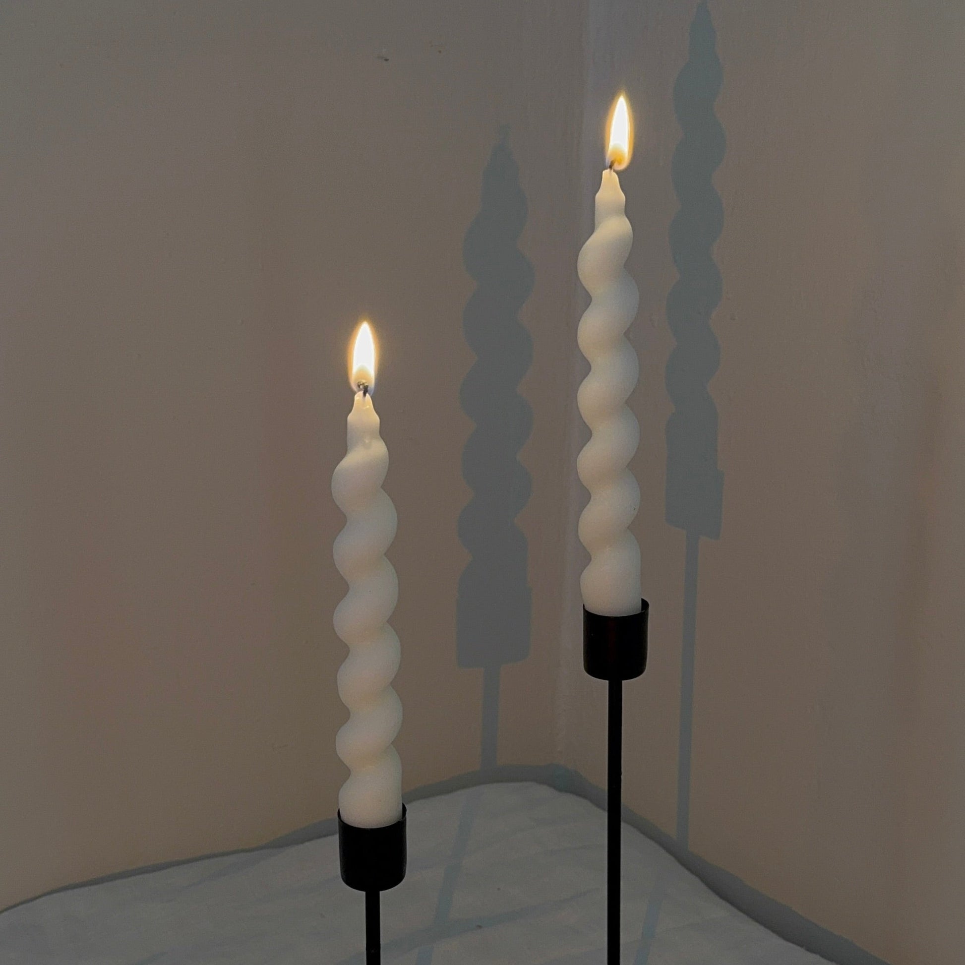 Two spiral candle holders with lit candles on a neutral background
