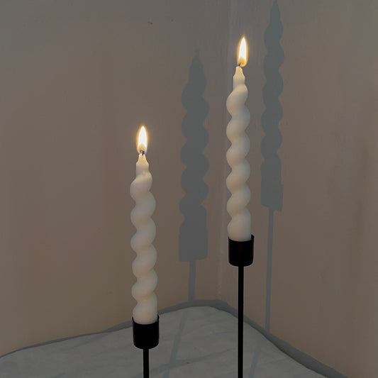 Two spiral candle holders with lit candles on a neutral background