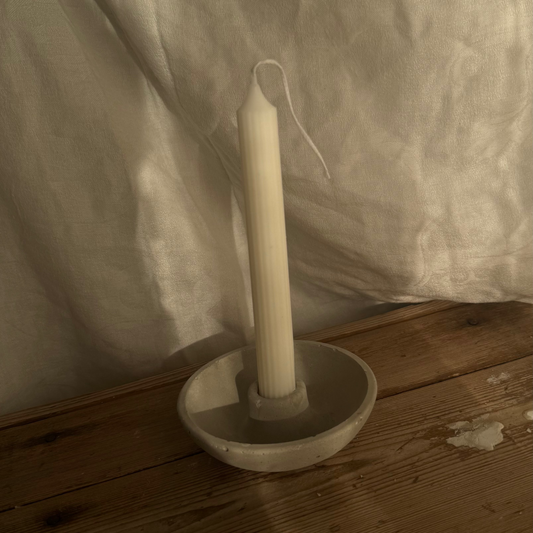 White candle in a holder on a wooden surface with a white curtain in the background