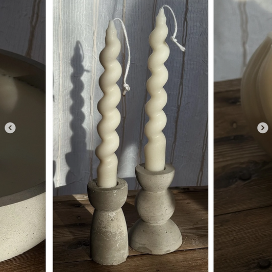 Two twisted candles in concrete candle holders on a wooden surface.