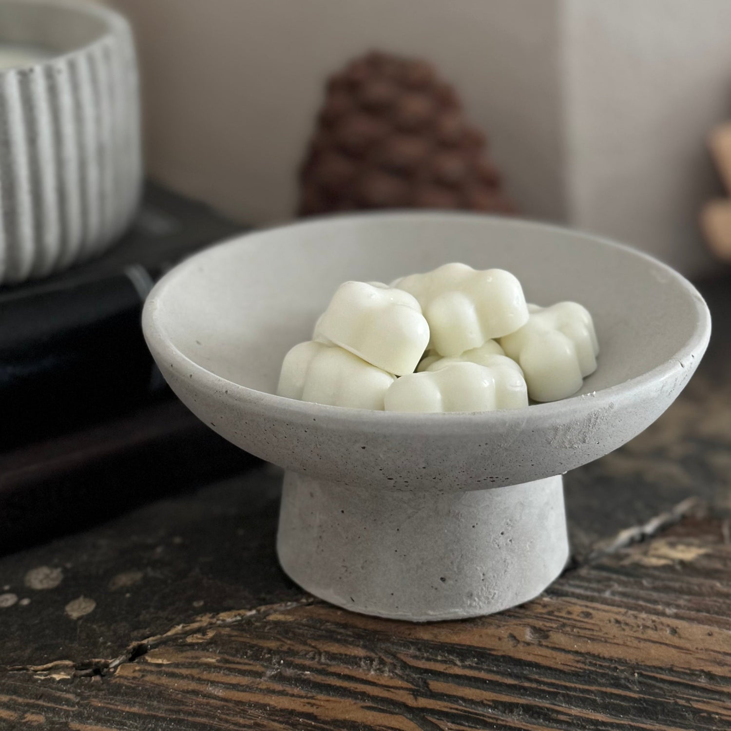 A minimalist concrete ring holder that doubles as a wax melt holder, displayed on a wooden surface.